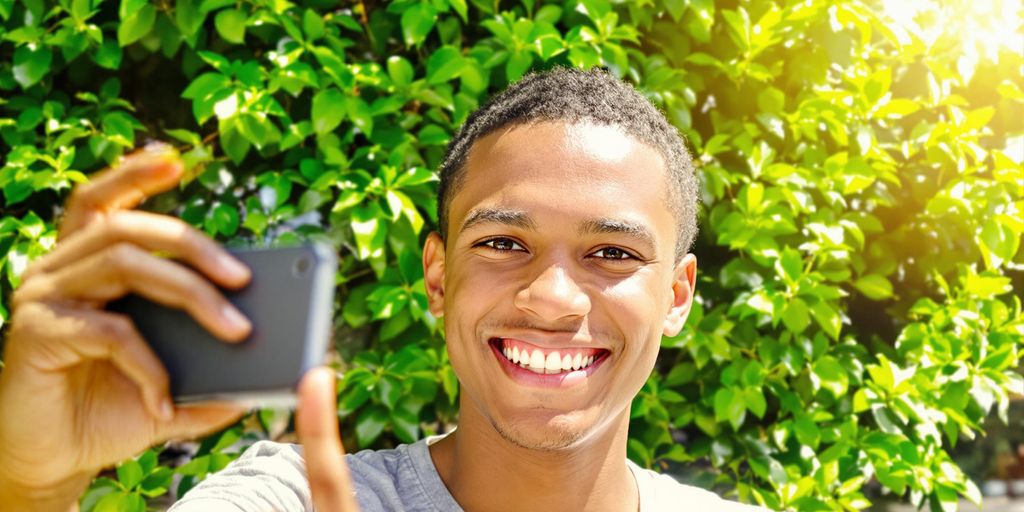 Person smiling, recording video outdoors.