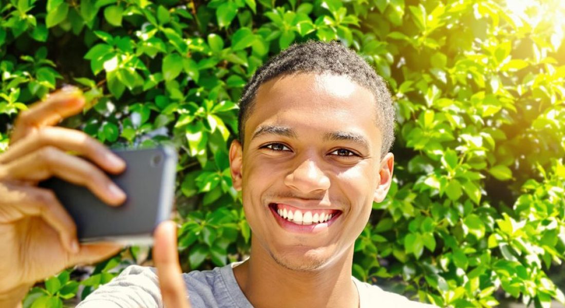 Person smiling, recording video outdoors.